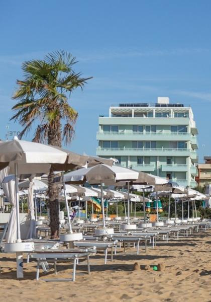 Spiaggia con ombrelloni e lettini, palme e edifici sullo sfondo.