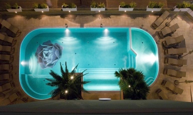 Piscina illuminata di notte con disegno floreale sul fondo.