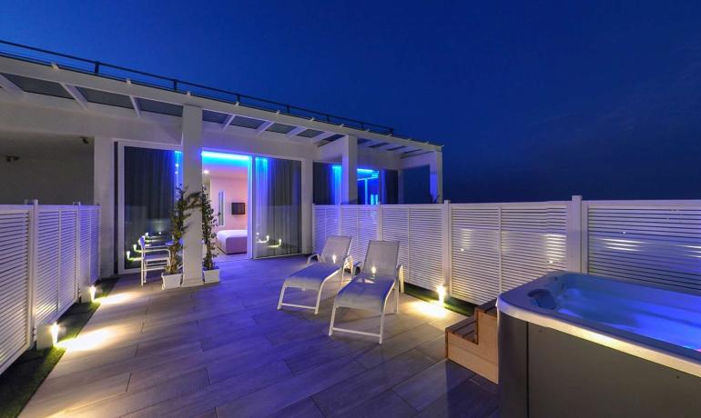 Terrazza moderna con lettini, jacuzzi e luci blu.