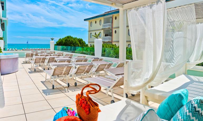 Terrazza soleggiata con lettini, vista mare e piscina.