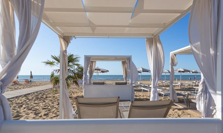 Spiaggia con lettini sotto gazebo bianchi, mare calmo.