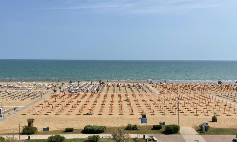 Spiaggia con ombrelloni arancioni e bianchi, mare calmo e cielo sereno.