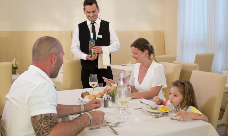 Family dining with waiter serving wine.