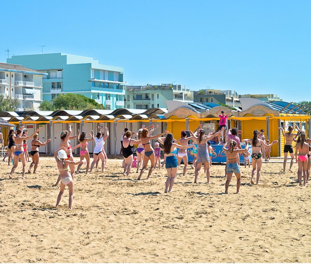 Persone fanno esercizi di gruppo sulla spiaggia, sotto il sole.