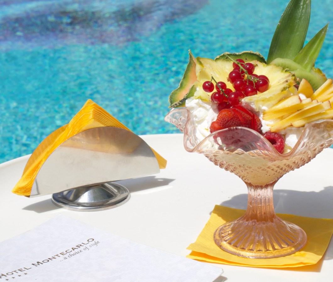 Coppa di frutta fresca e panna su tavolo a bordo piscina.