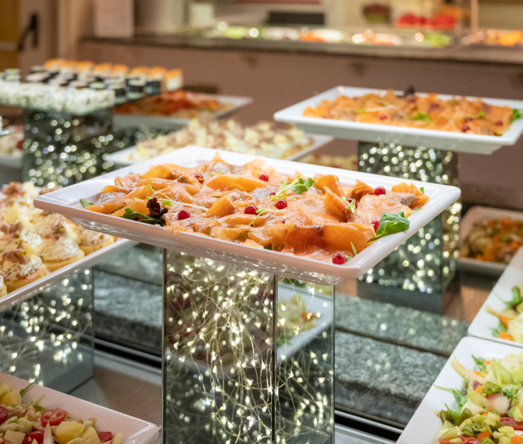 Buffet elegante con piatti di salmone affumicato e antipasti vari su alzate illuminate.