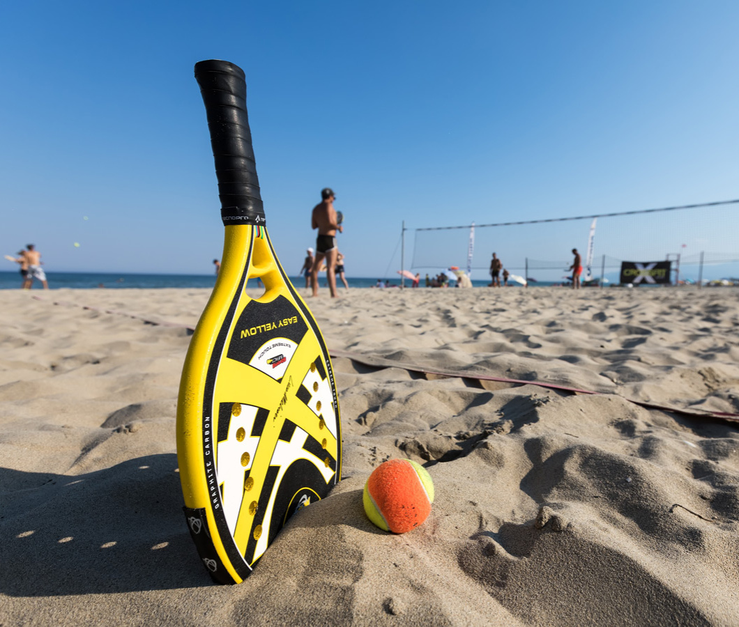 Beach-Tennis-Schläger auf Sand mit Netz im Hintergrund.