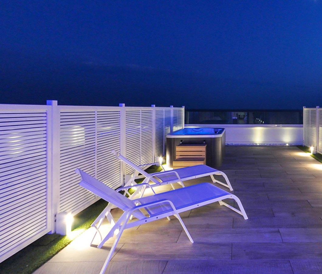 Terrazza con lettini e vasca idromassaggio, illuminata di notte.