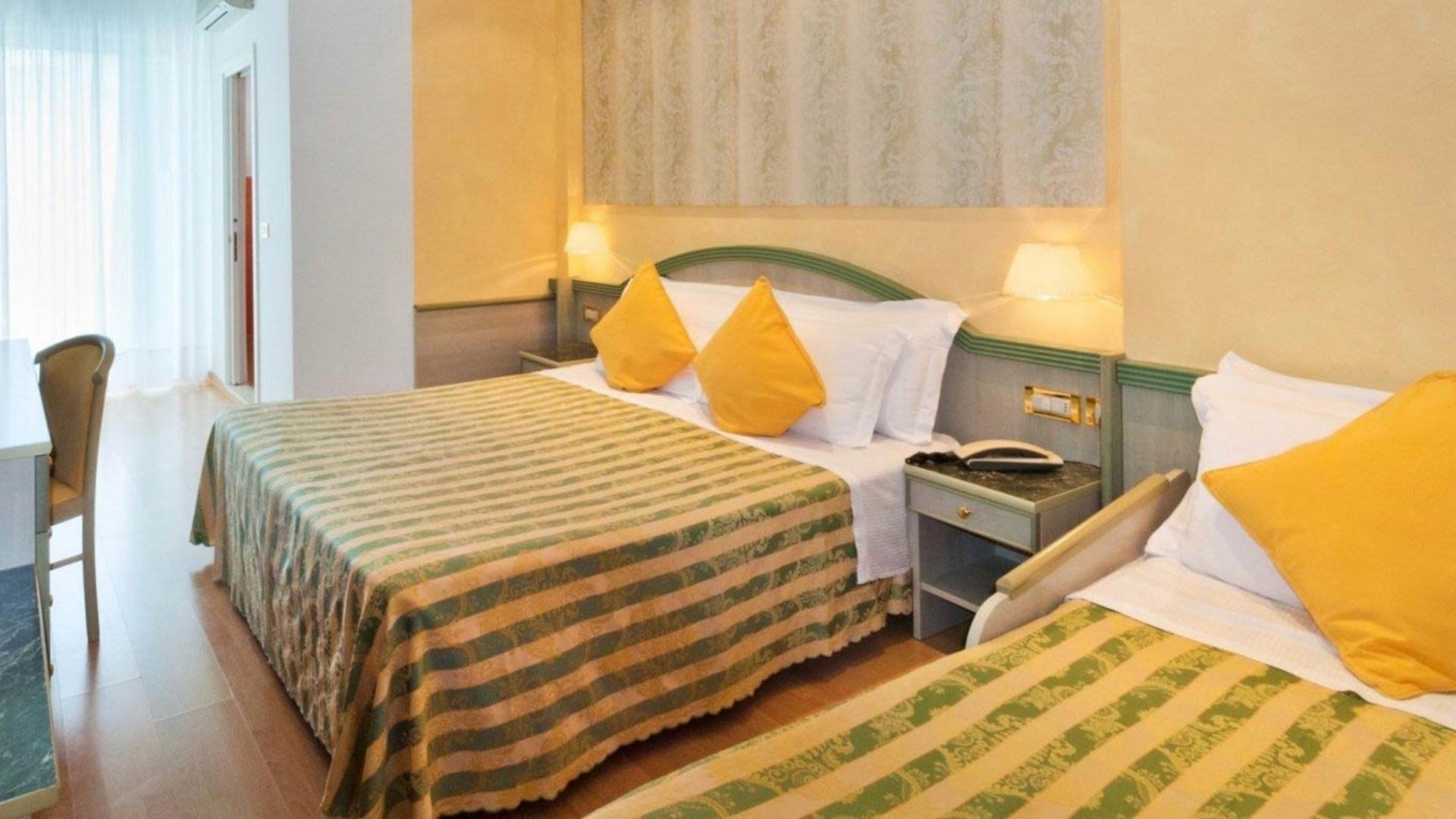 Camera d'albergo con due letti e cuscini gialli.
