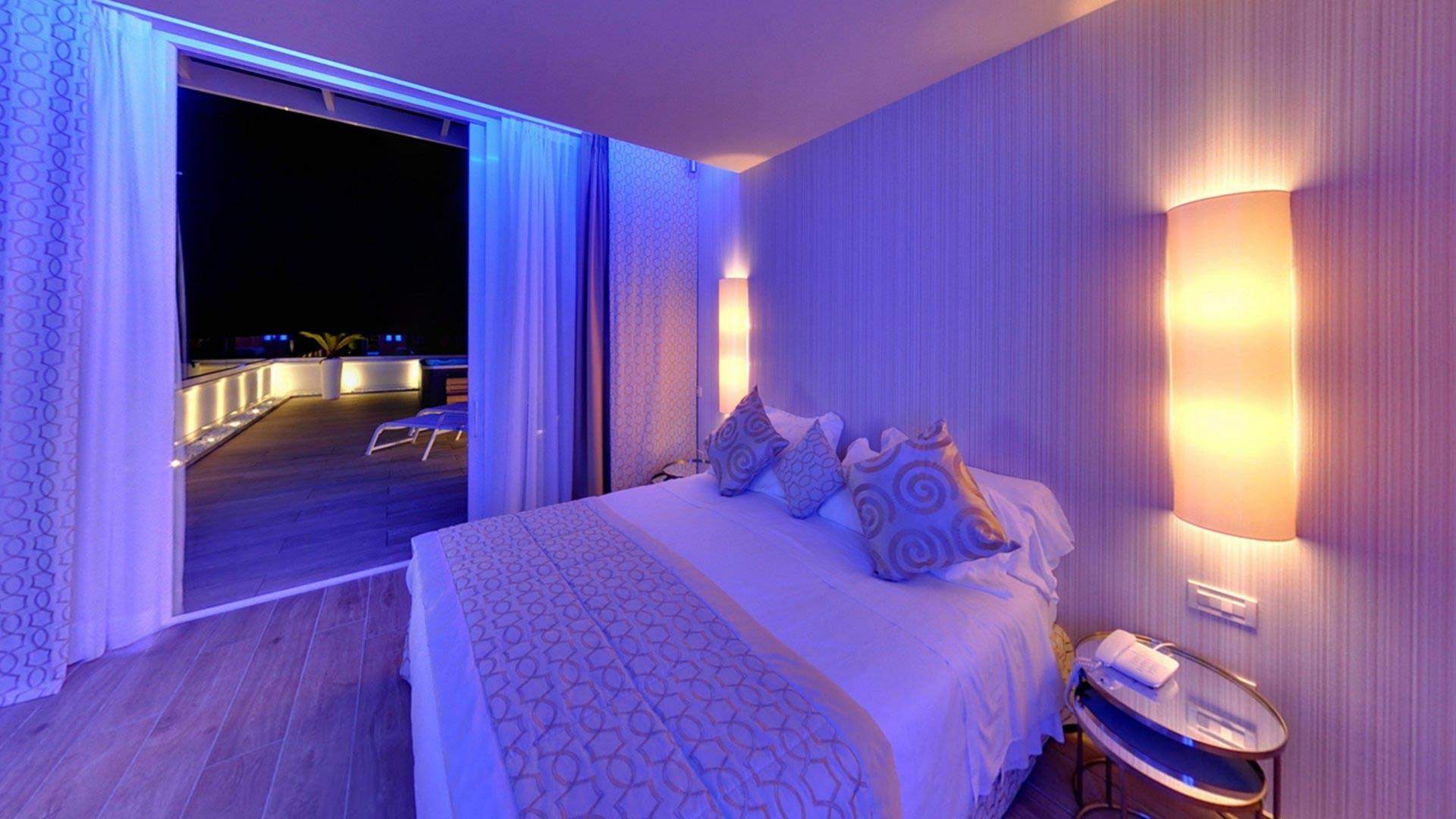 Camera moderna con letto e terrazza illuminata di notte.