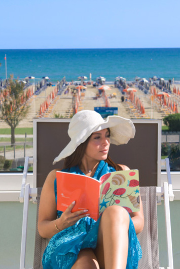 Donna legge in spiaggia con cappello bianco.