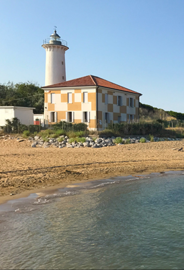 Faro e casa su spiaggia sabbiosa con mare calmo sotto cielo sereno.