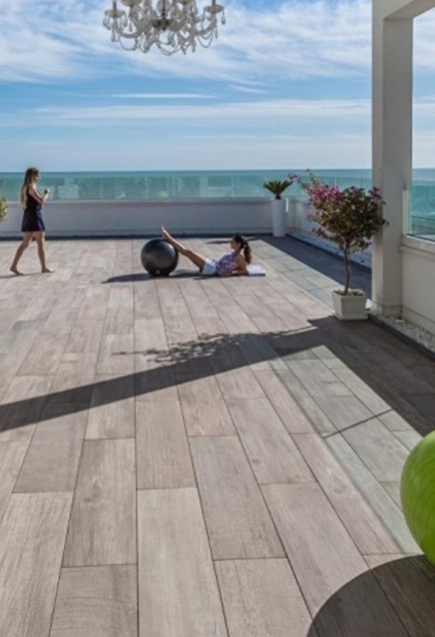 Terrazza con vista mare, pavimento in legno, persone che si rilassano.