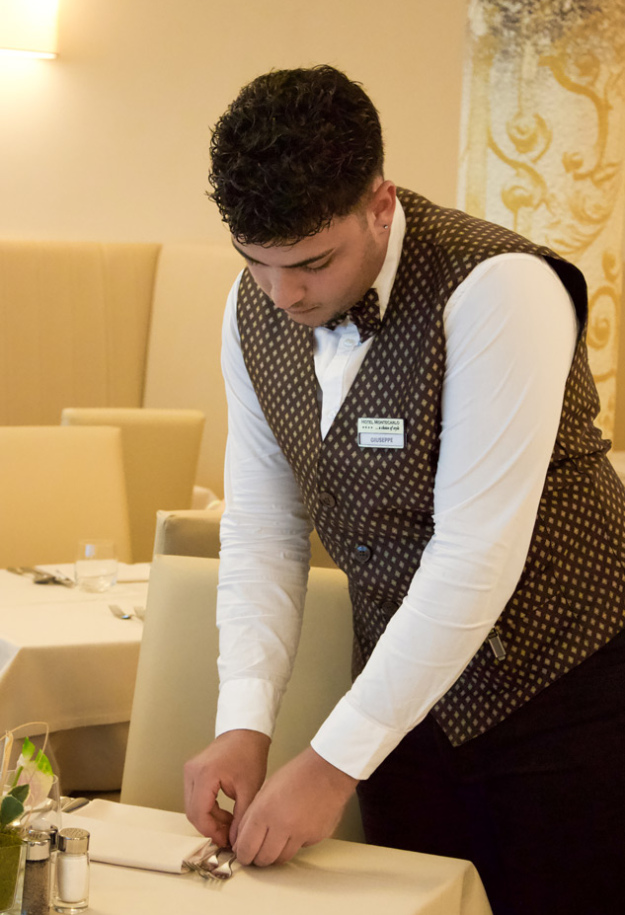 Cameriere prepara un tavolo in un elegante ristorante, indossando un gilet a quadri.