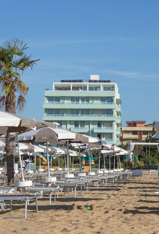 Spiaggia sabbiosa con ombrelloni e palme, hotel sullo sfondo.