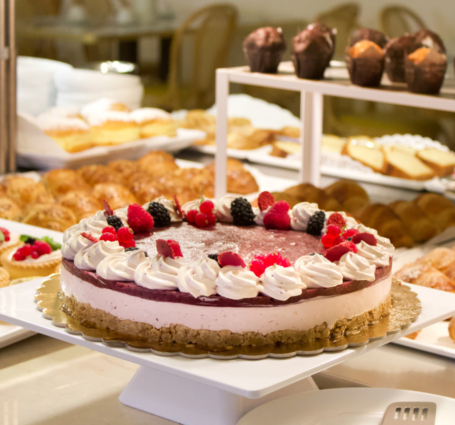 Torta ai frutti di bosco con panna, circondata da dolci e croissant.
