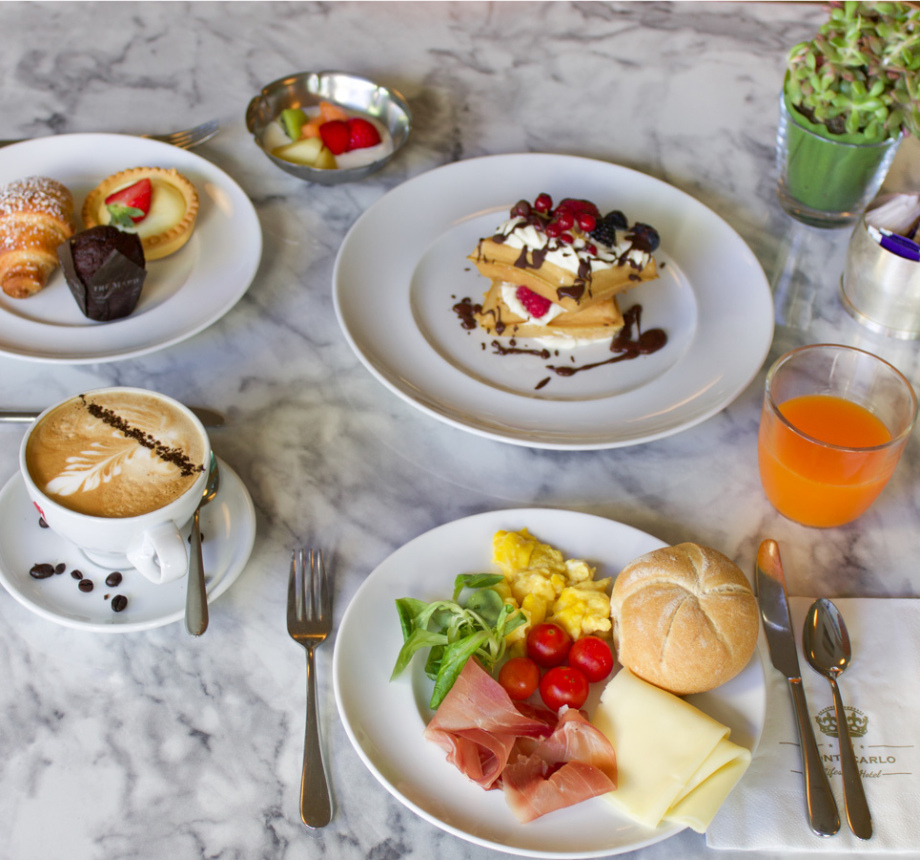 Colazione con dolci, frutta, uova, prosciutto, formaggio, cappuccino e succo d'arancia.
