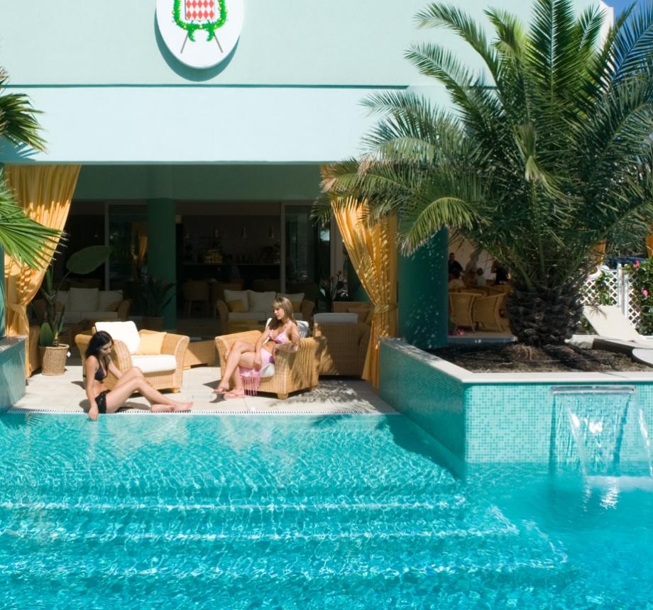 Due donne rilassate a bordo piscina con palme.